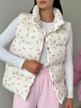 Person wearing a floral patterned puffer vest over a white shirt and pink pants.